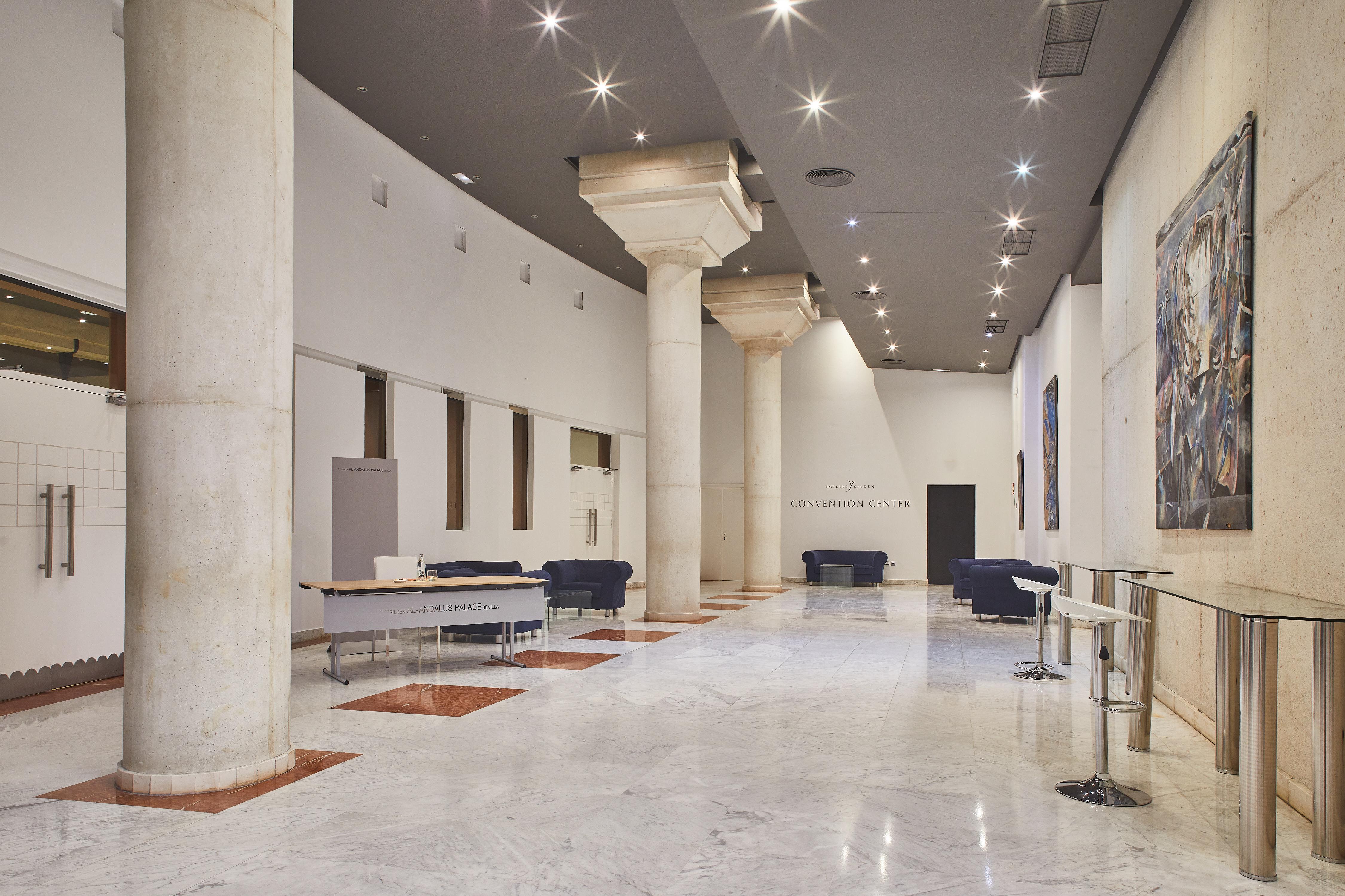 Silken Al-Andalus Palace Sevilla Exterior foto The photo shows a spacious interior, possibly a lobby or gallery, characterized by high ceilings and white walls. Large, cylindrical columns are present, supporting the structure. The floor appears to be made of polished marble, enhancing the sense o